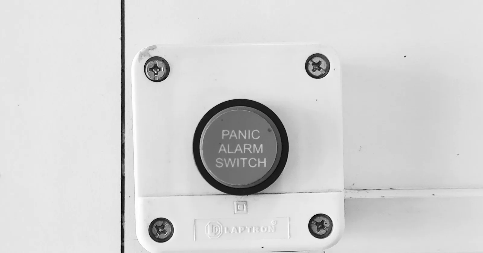 A panic alarm switch mounted on an office wall, shown in black and white